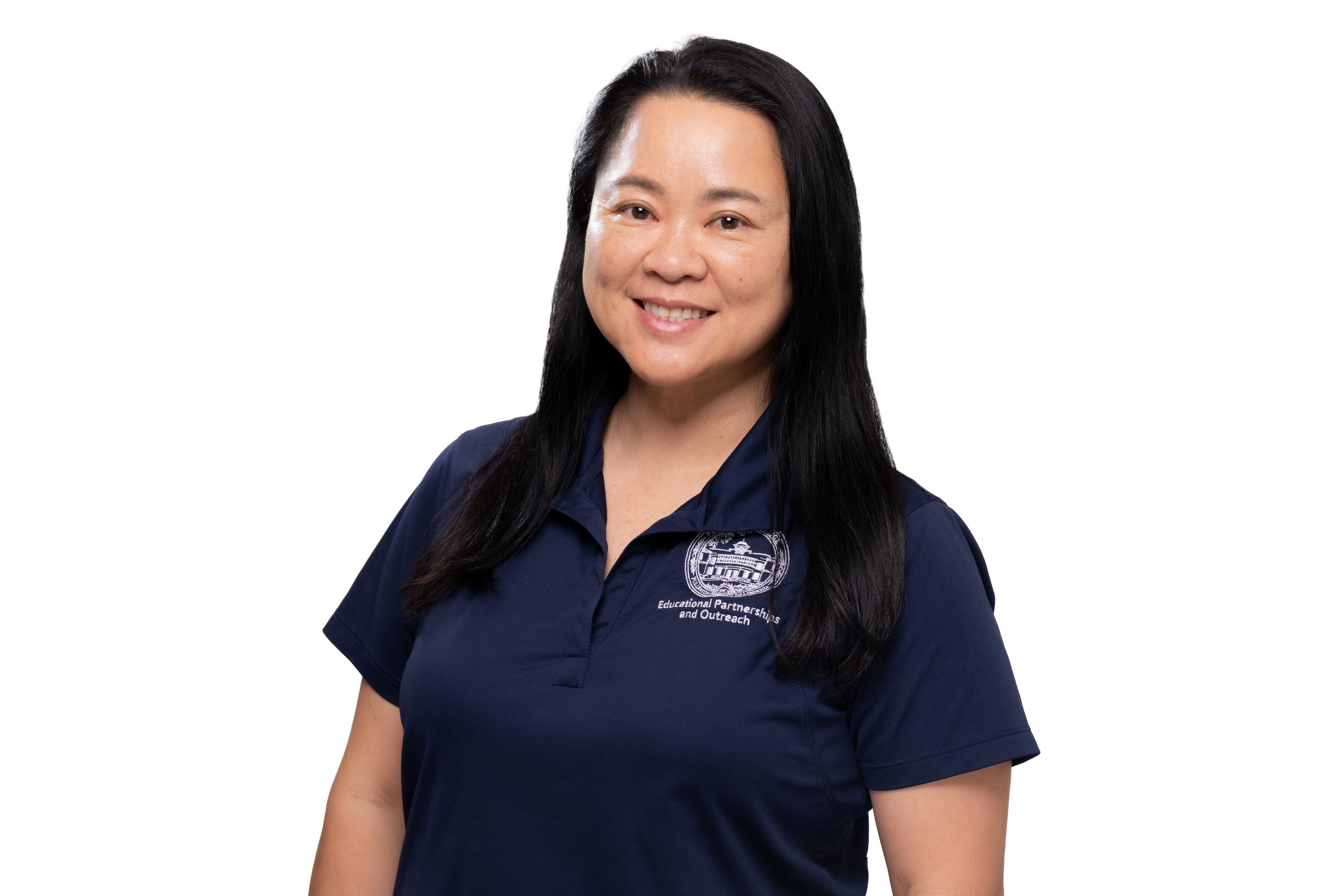 A person with long dark hair smiles while wearing a navy blue polo shirt featuring an embroidered logo and text.