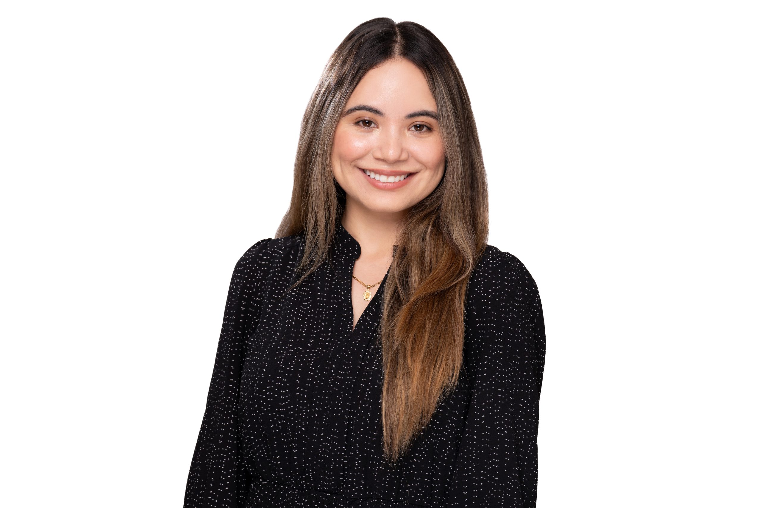 A person with long brown hair smiles warmly while wearing a black speckled top against a plain white background.