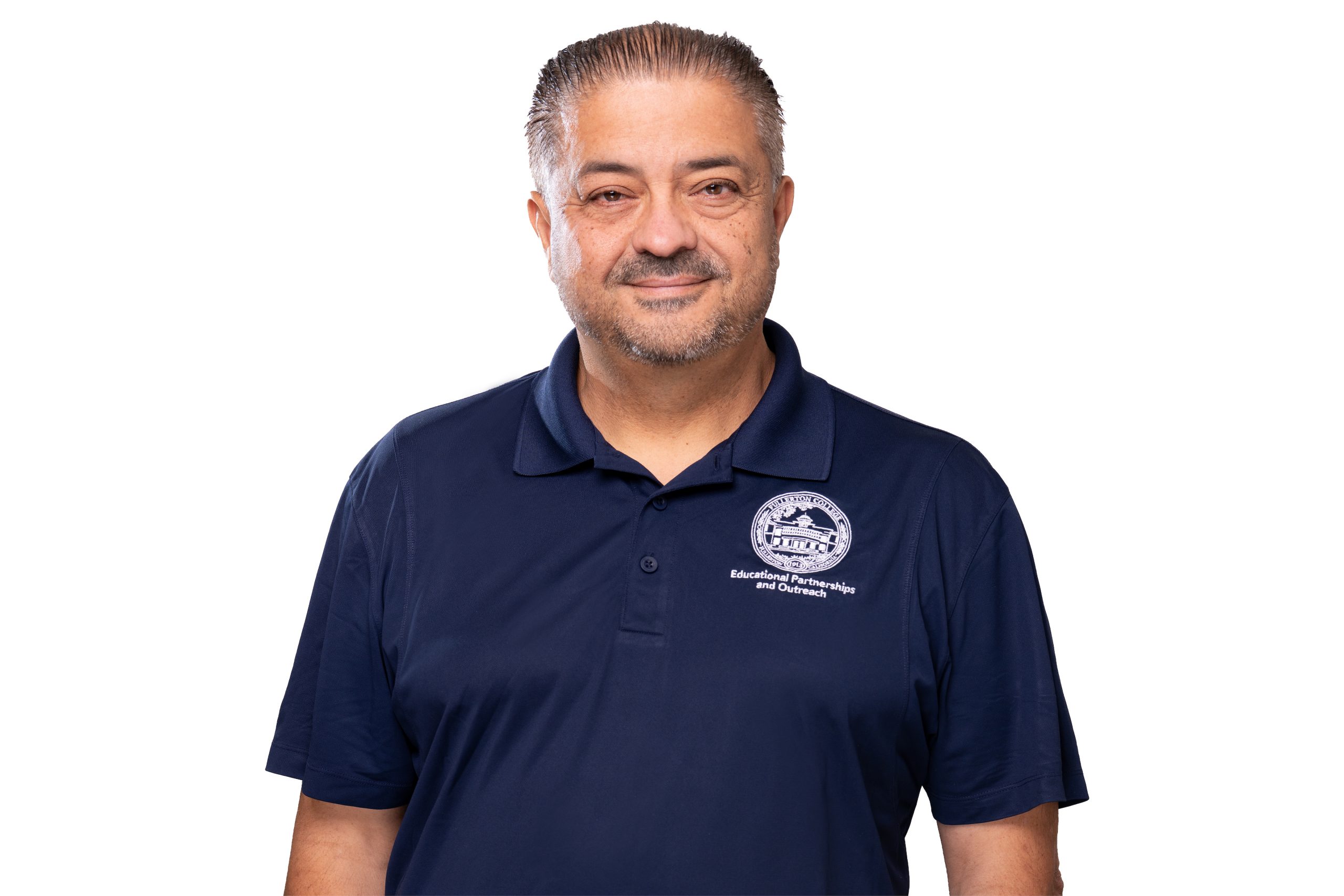 A person with neatly styled hair and a beard smiles while wearing a navy blue polo shirt featuring a logo and text.