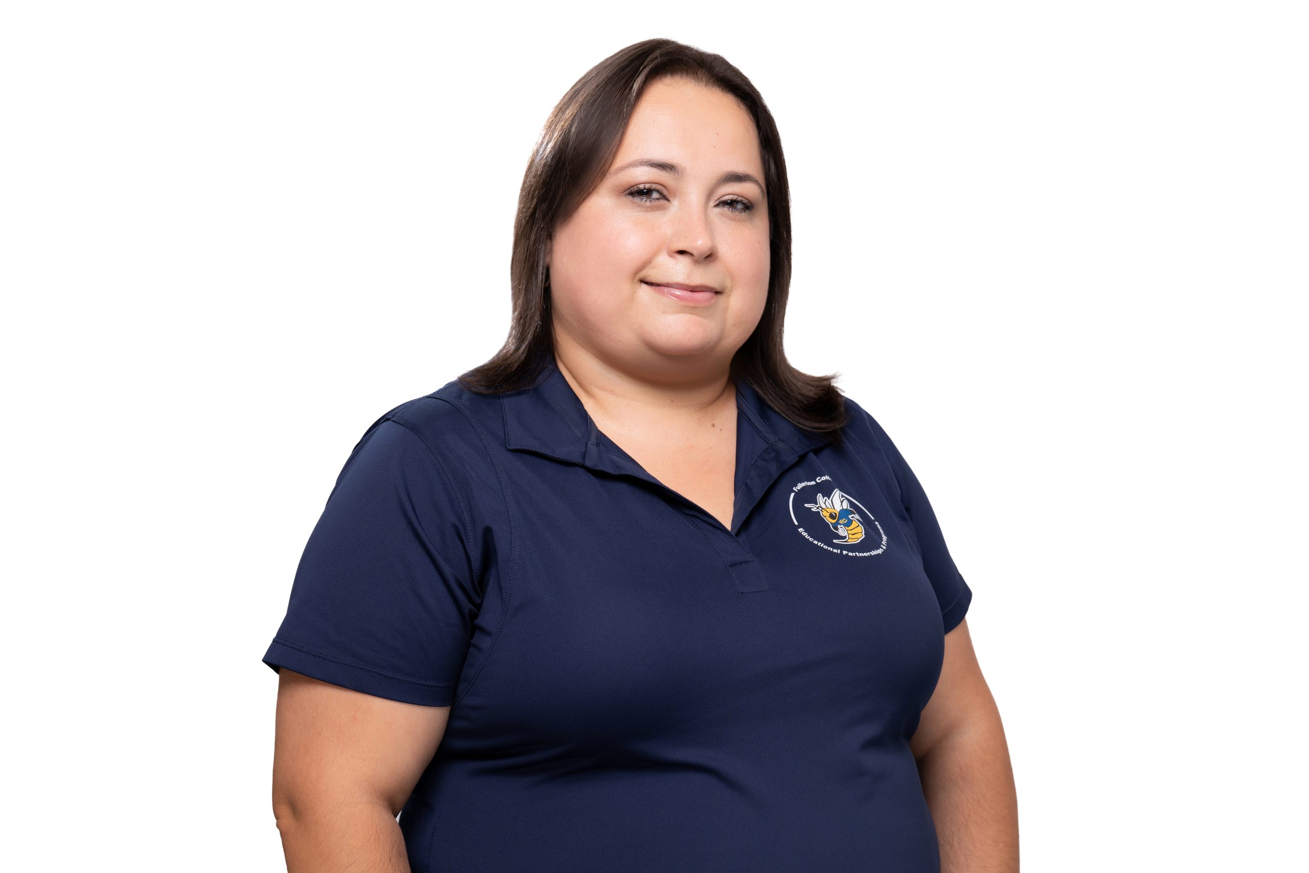 A person with shoulder-length brown hair smiles while wearing a navy blue polo shirt featuring a circular logo on the left chest.